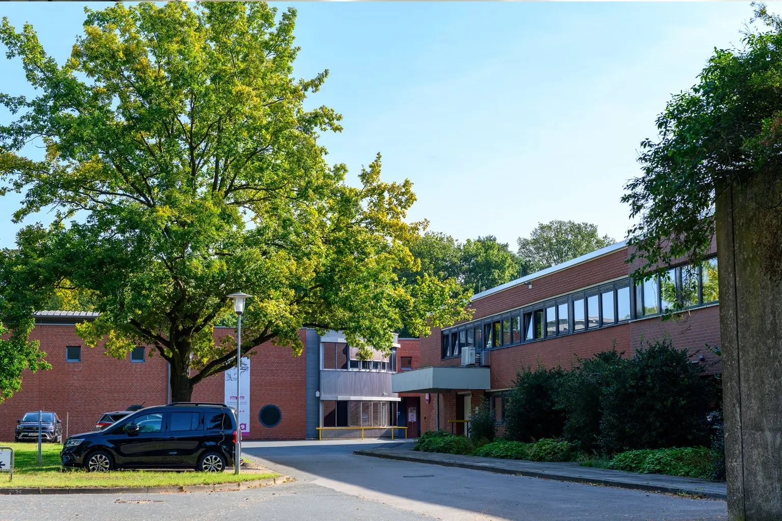 Außenansicht eines modernen Ziegelgebäudes mit viel Grün und einem geparkten Auto.