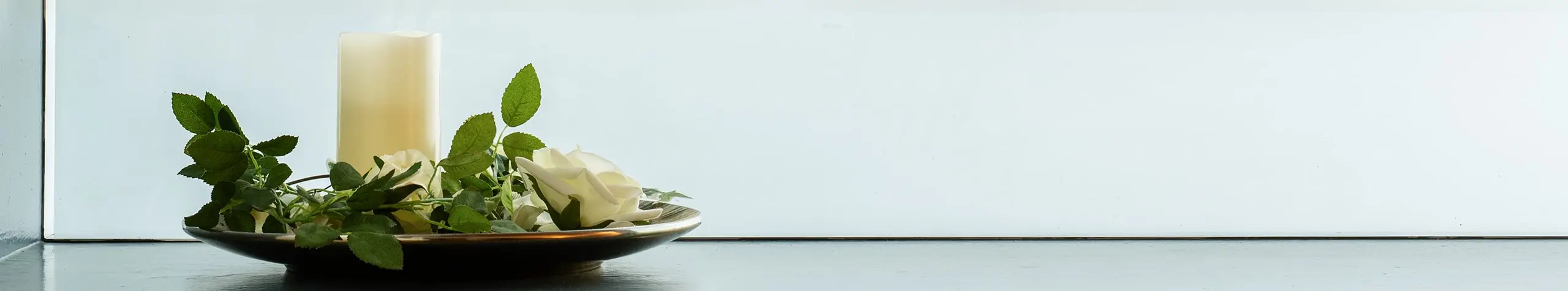 Weiße Kerze und Rosen in einer Dekoschale.