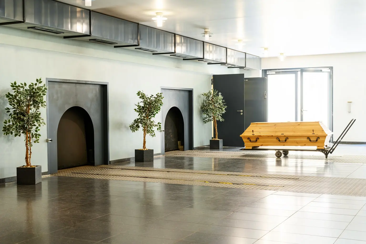Holzsarg auf Rollwagen in einem Krematoriumsraum vor den Einäscherungsöfen