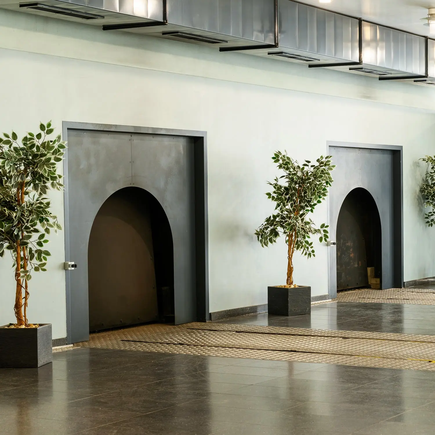 Zwei große, graue Ofentüren mit Rundbögen in einem modernen Krematorium, flankiert von Grünpflanzen.