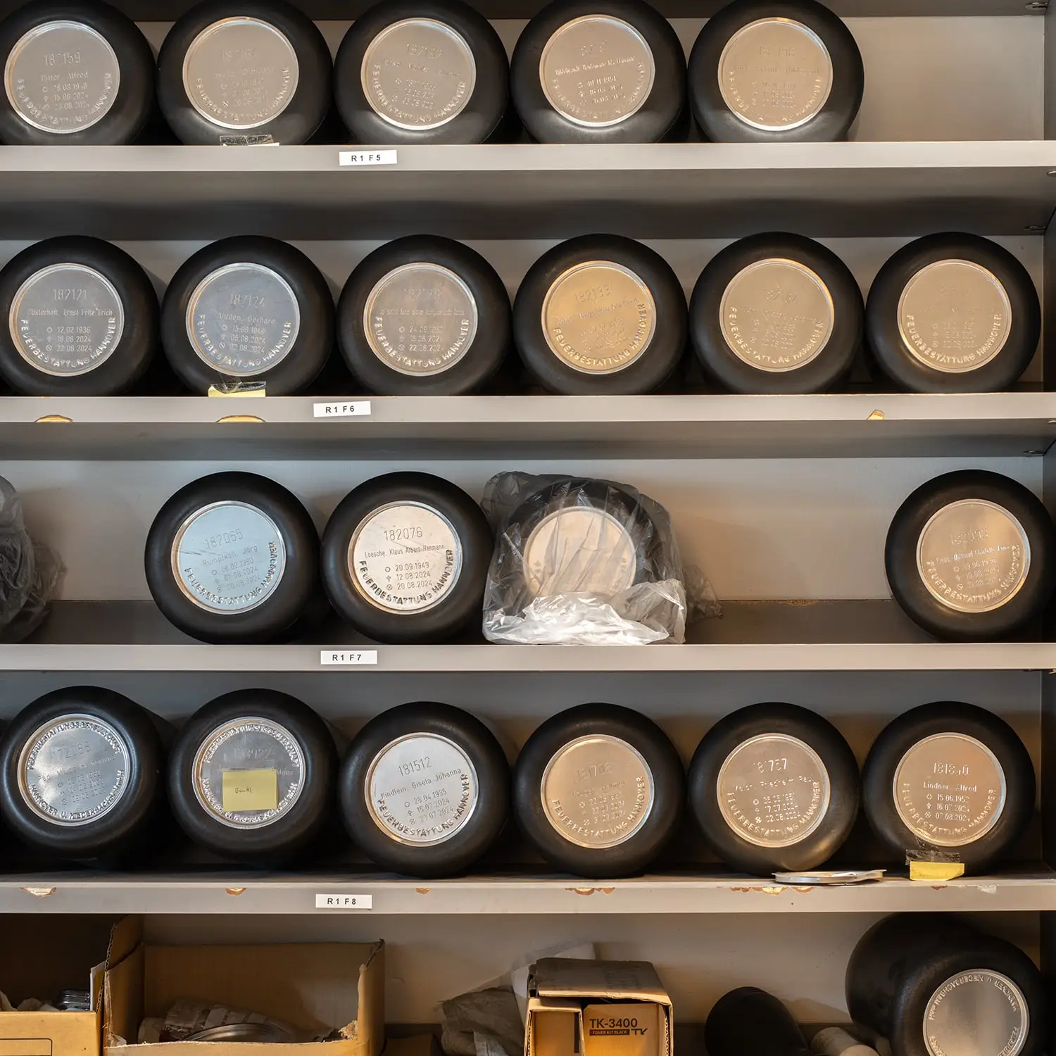 Reihen von Urnen mit eingravierten Namen und Daten im Lager eines Krematoriums.