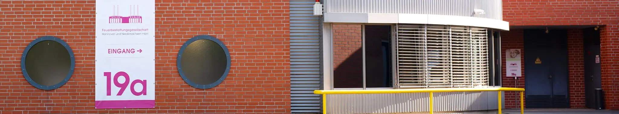 Gebäudeansicht der Feuerbestattungsgesellschaft Hannover und Niedersachsen mit Eingangsschild, Backsteinwand und Glasfassade